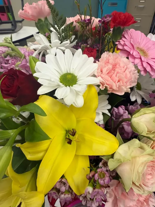 Close-up of a colorful flower arrangement including yellow lilies, white daisies, and pink carnations.