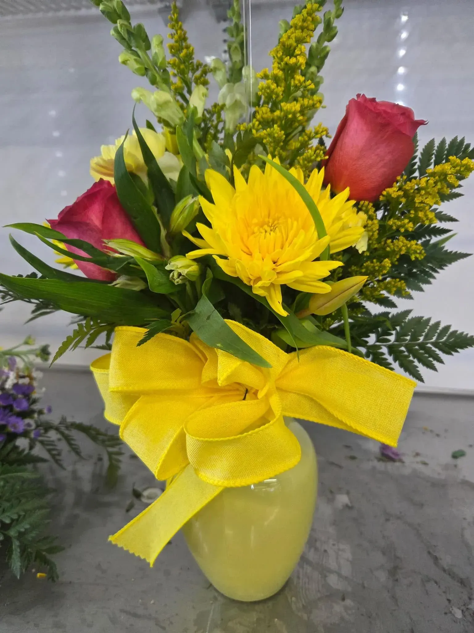 Yellow vase with yellow bow holding yellow daisy, two pink roses, and green foliage. Yellow vase with yellow bow holding yellow daisy, two pink roses, and green foliage.