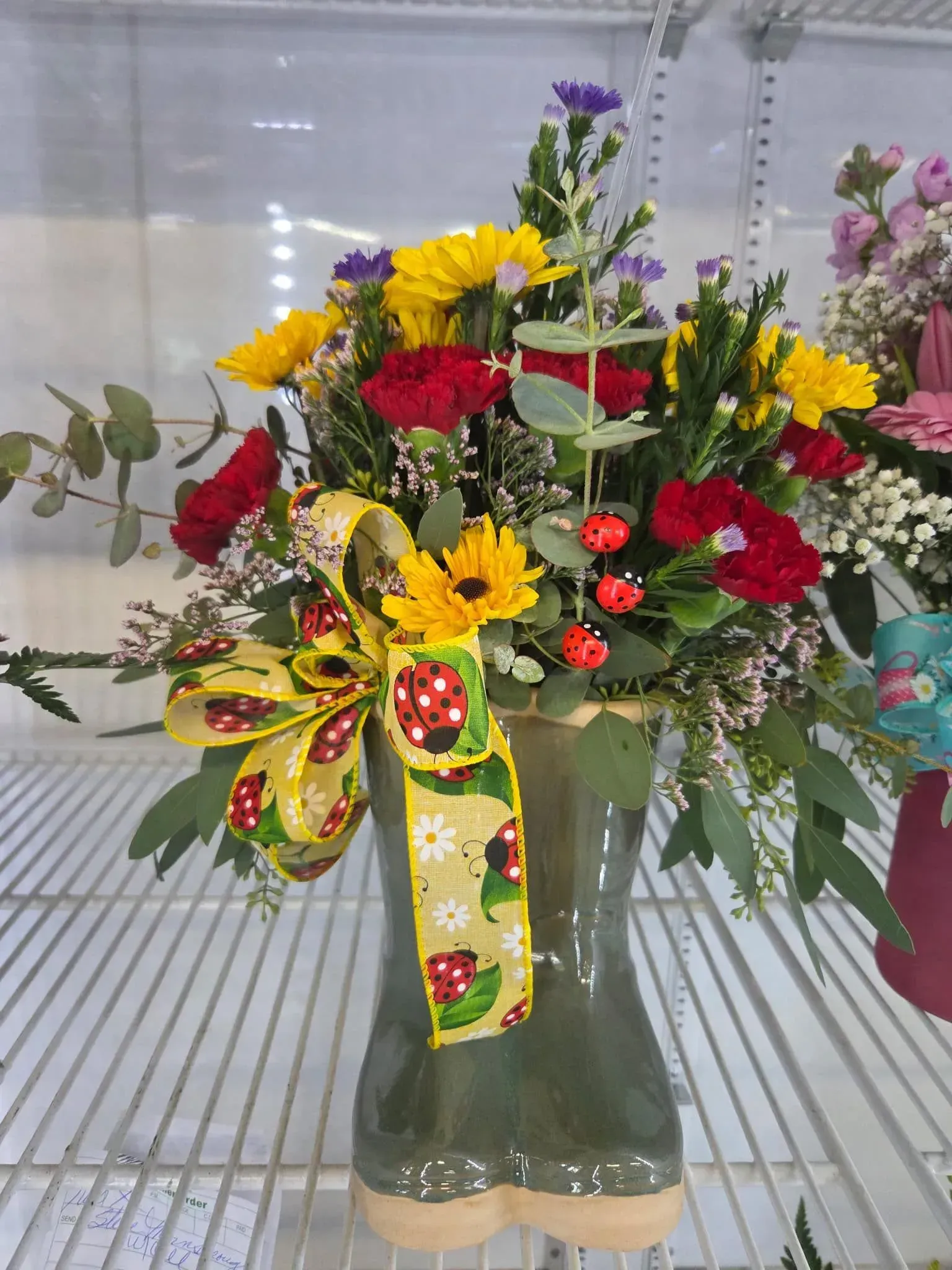 Floral arrangement in a green boot-shaped vase with red carnations, yellow sunflowers, and a ladybug ribbon. Floral arrangement in a green boot-shaped vase with red carnations, yellow sunflowers, and a ladybug ribbon.