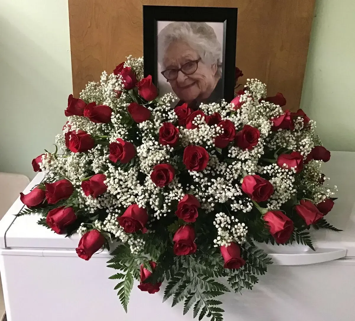 A floral arrangement of red roses and white filler with a photo in a black frame.