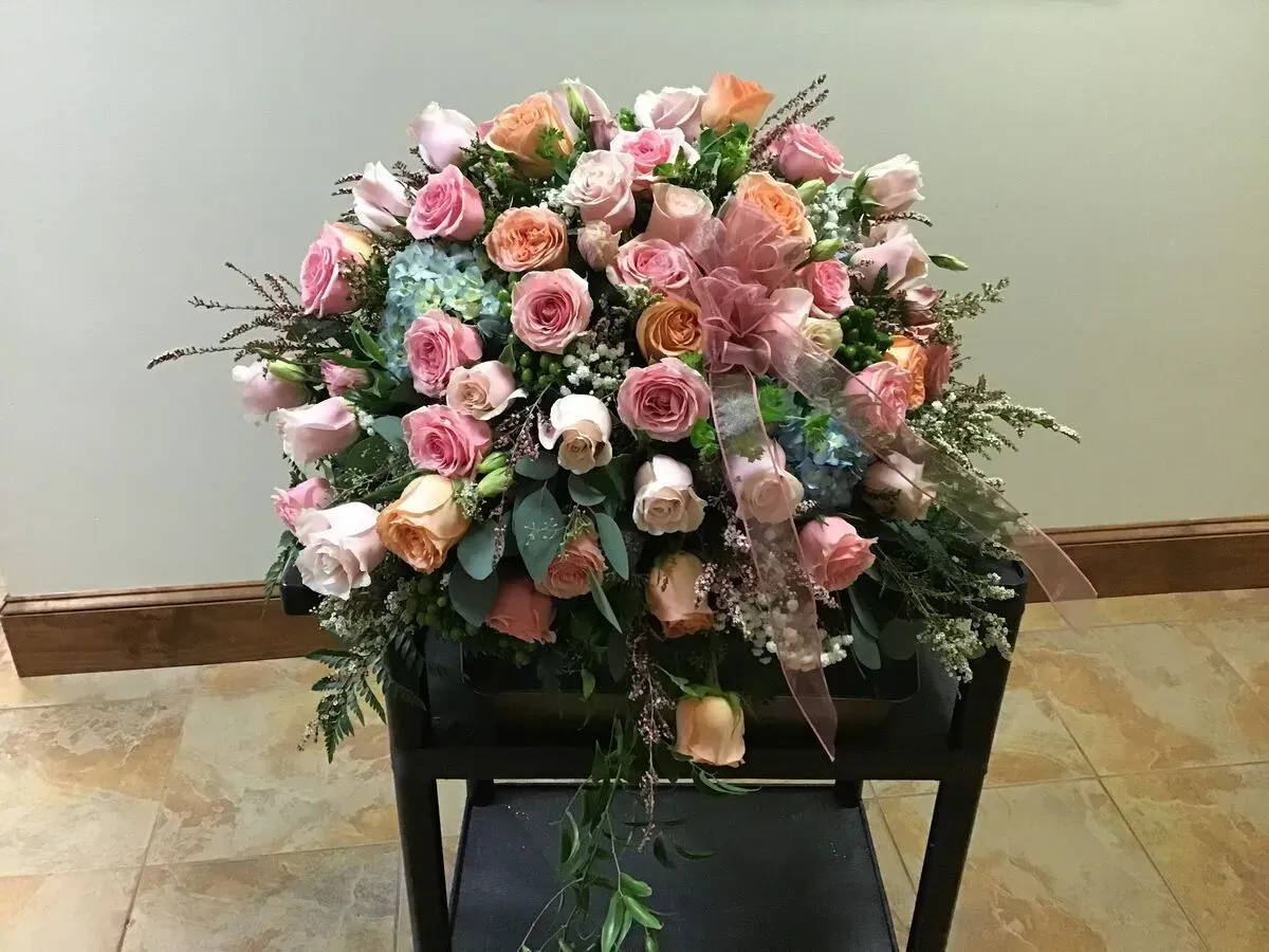 Floral arrangement of pink, peach, and cream roses with greenery and ribbon on a dark chair.