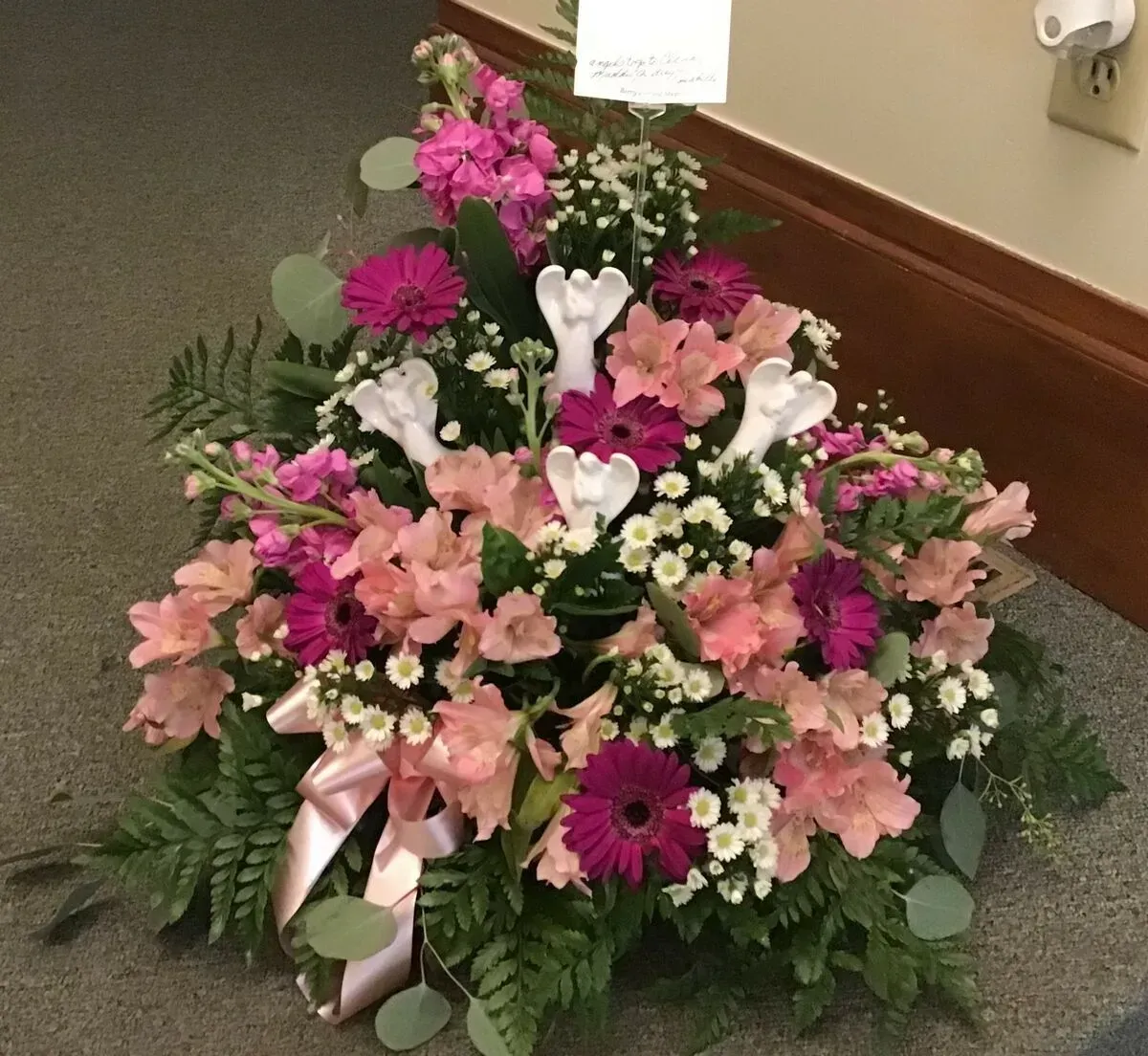 Floral arrangement with pink and magenta flowers, greenery, and a light pink bow.