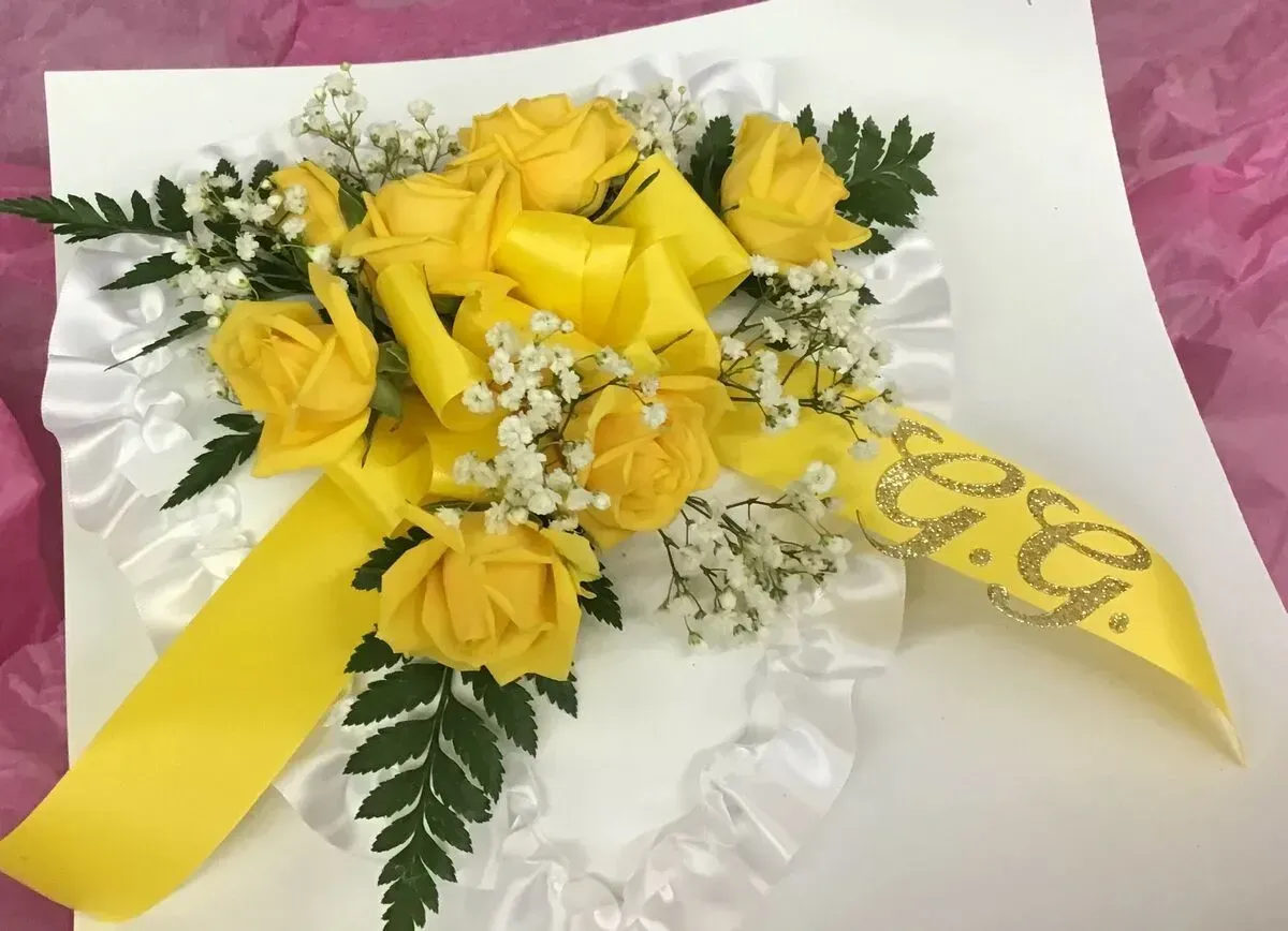 Yellow rose and baby's breath floral arrangement on a white heart with a yellow ribbon.