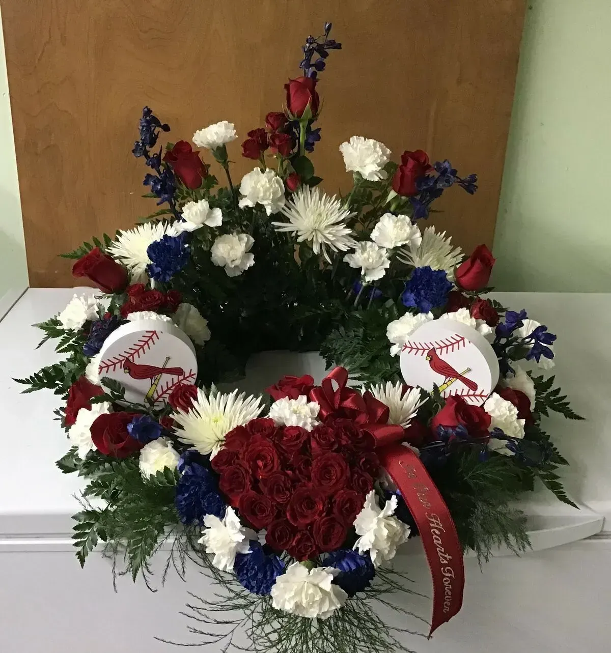 Floral wreath with red roses, white carnations, blue flowers, and two baseball-themed embellishments.