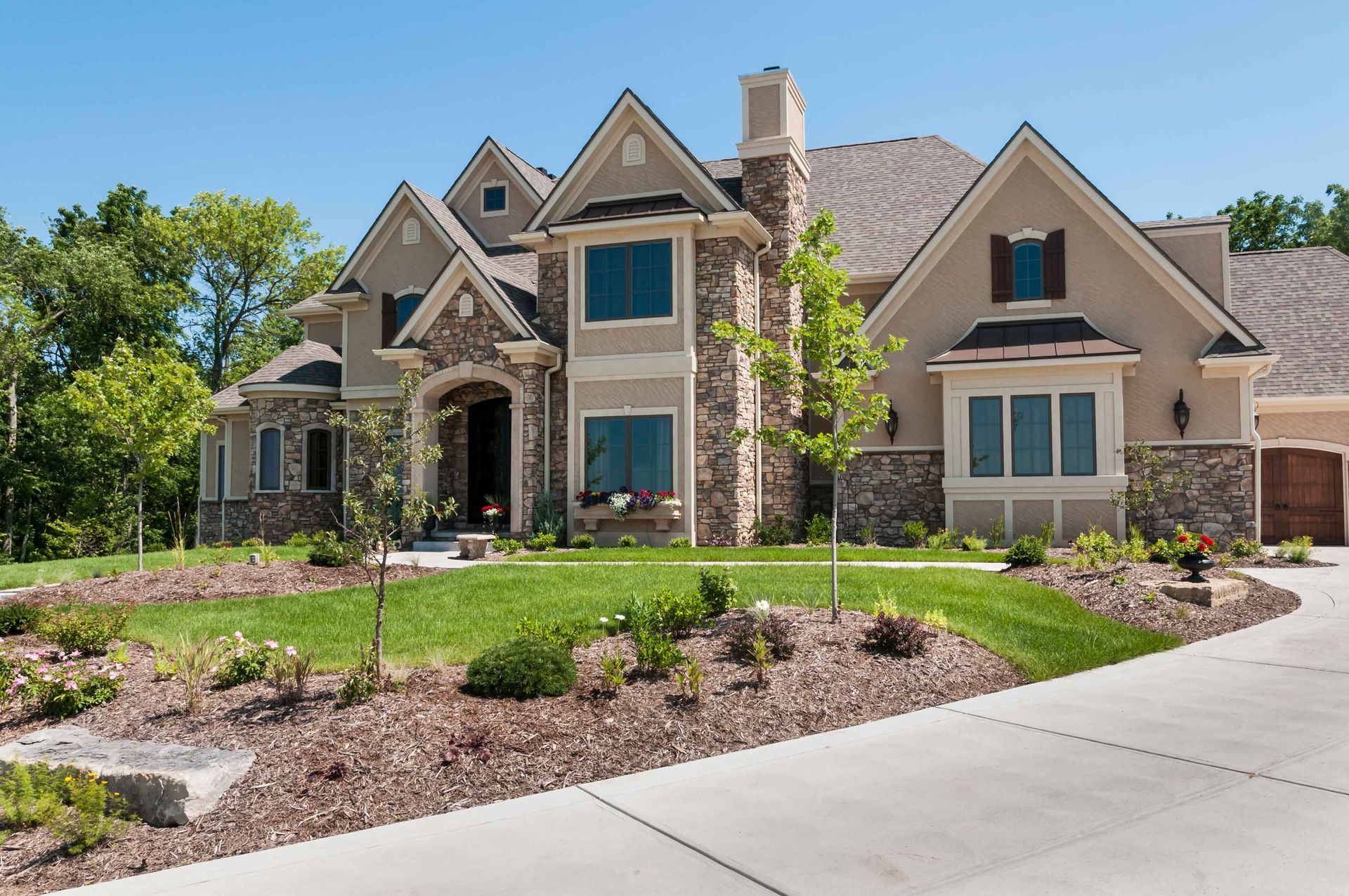 Large beige and stone house with a lush green lawn, driveway, and blue sky. Large beige and stone house with a lush green lawn, driveway, and blue sky.