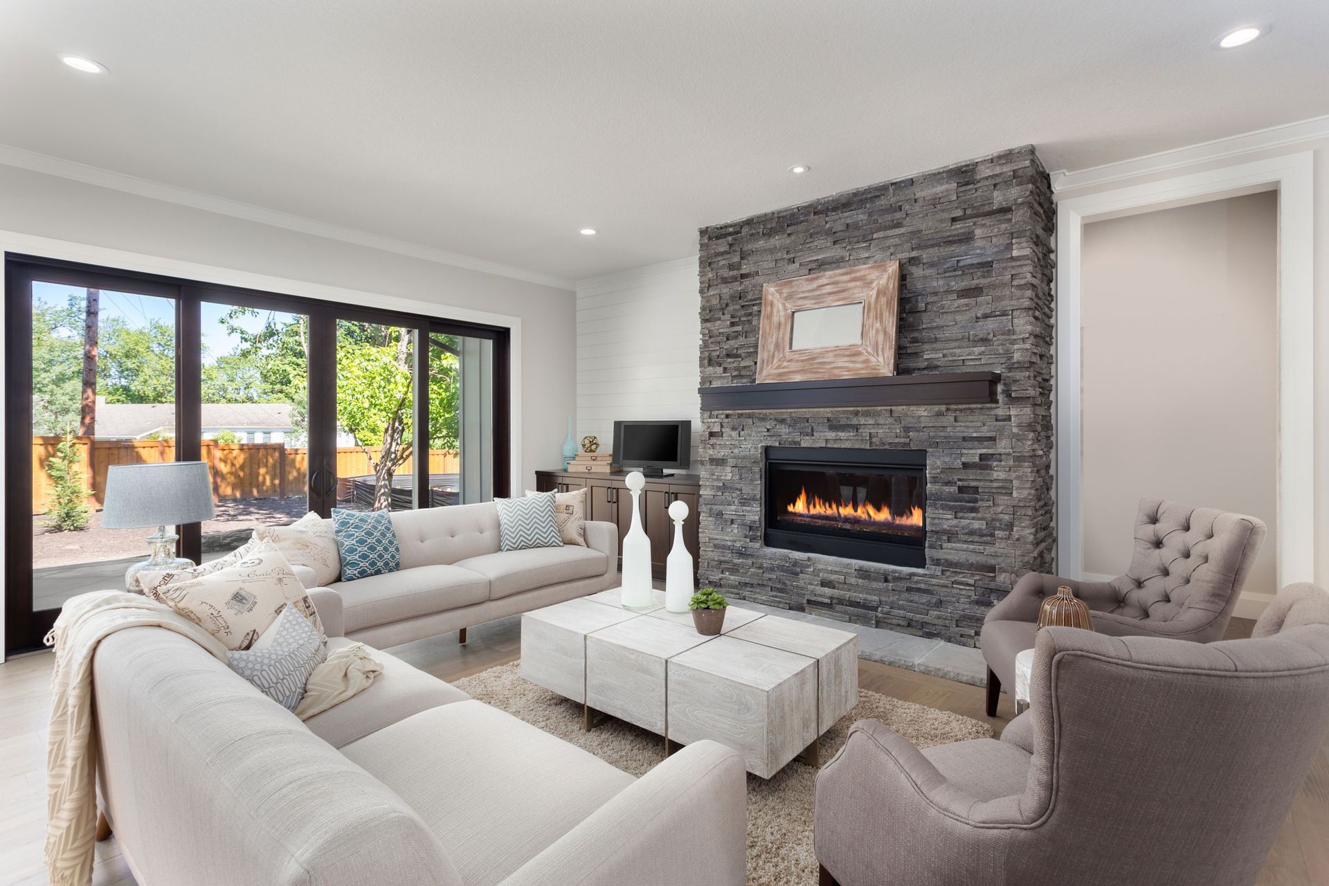 Living room with stone fireplace, sliding glass door, neutral-toned furniture. 