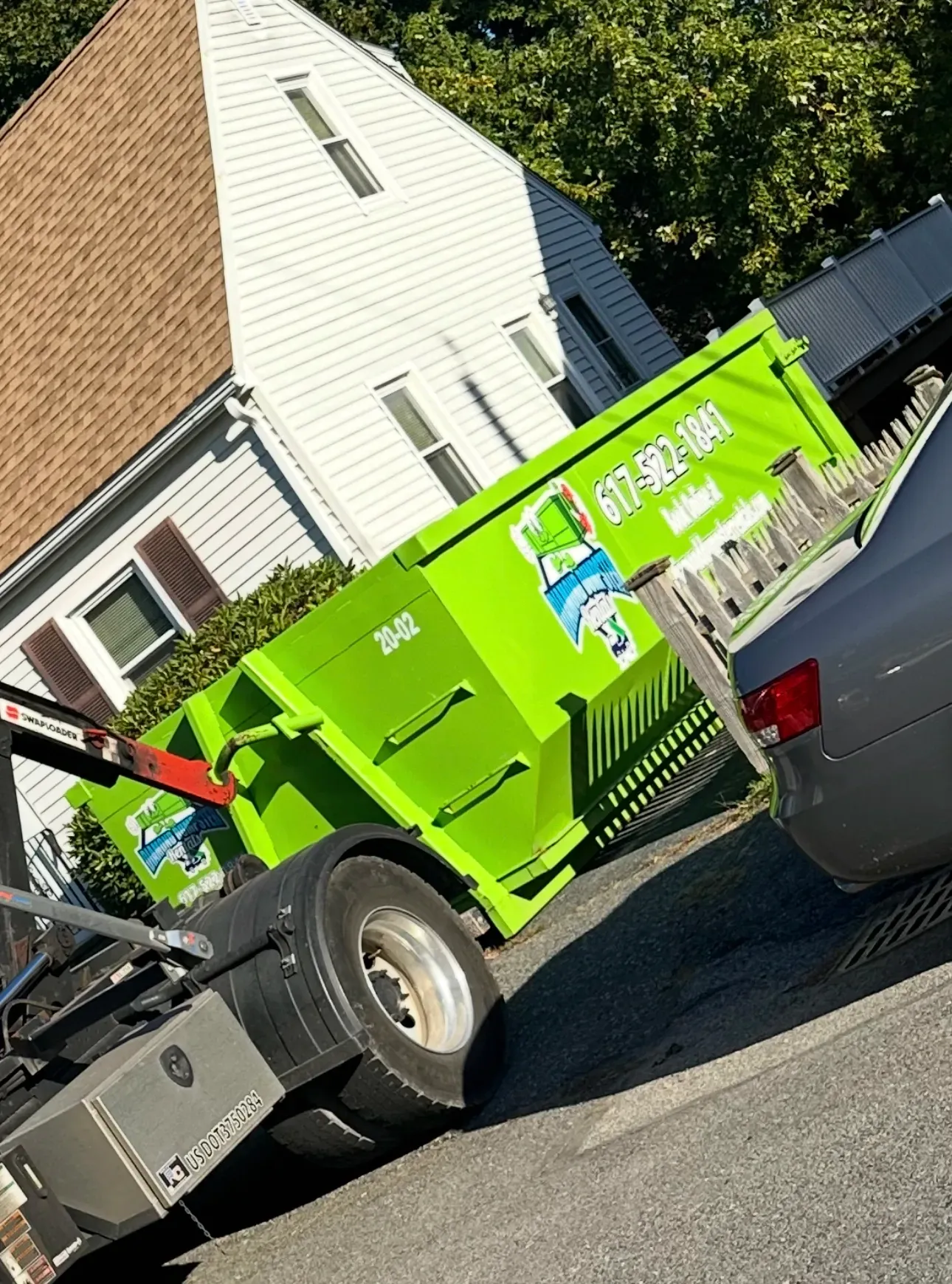 A green dumpster is sitting on the side of the road next to a car.