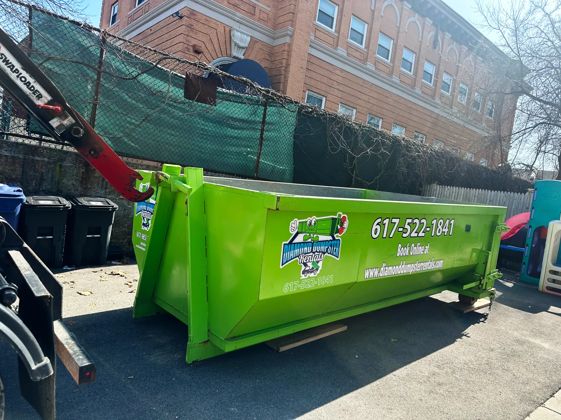 A green dumpster is parked in front of a brick building.