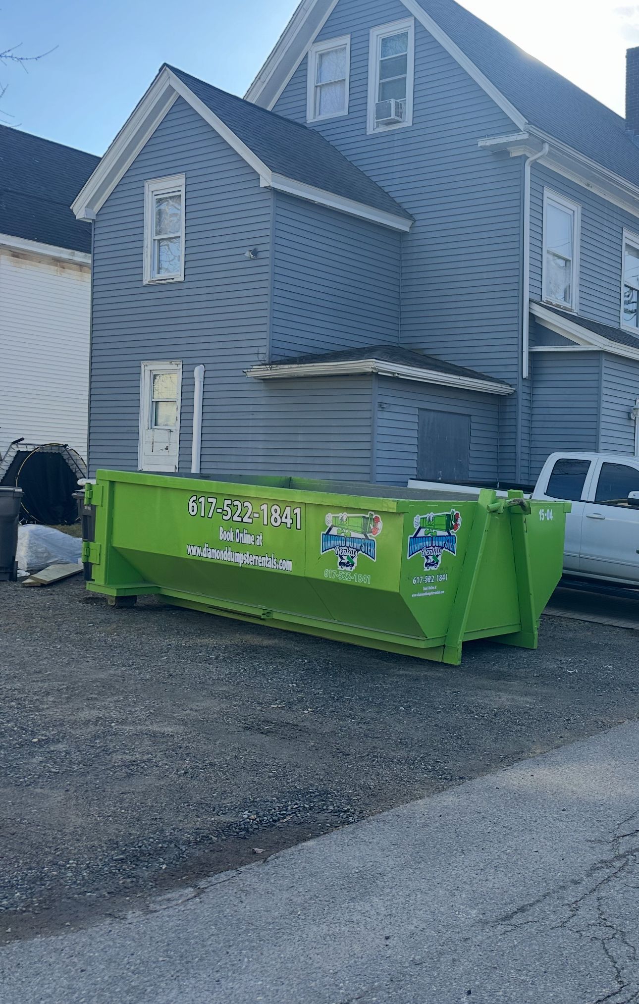 A green dumpster is parked in front of a house.