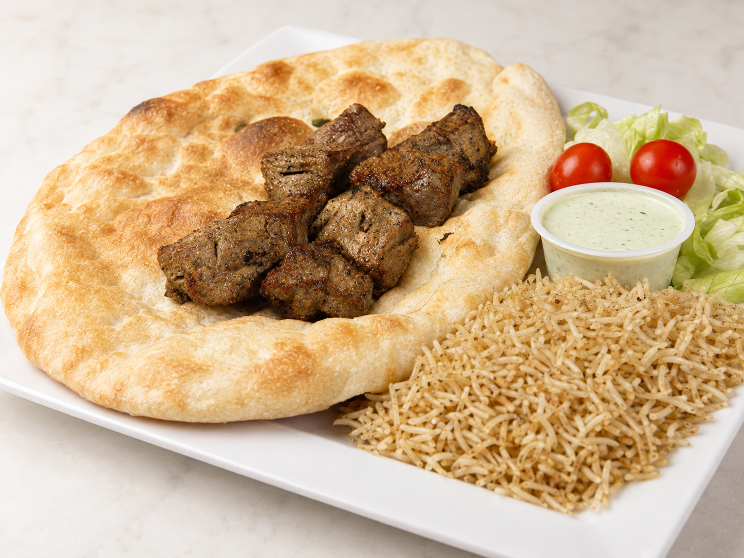 Plate of grilled meat with pita, rice, green sauce, and tomatoes on a white tray