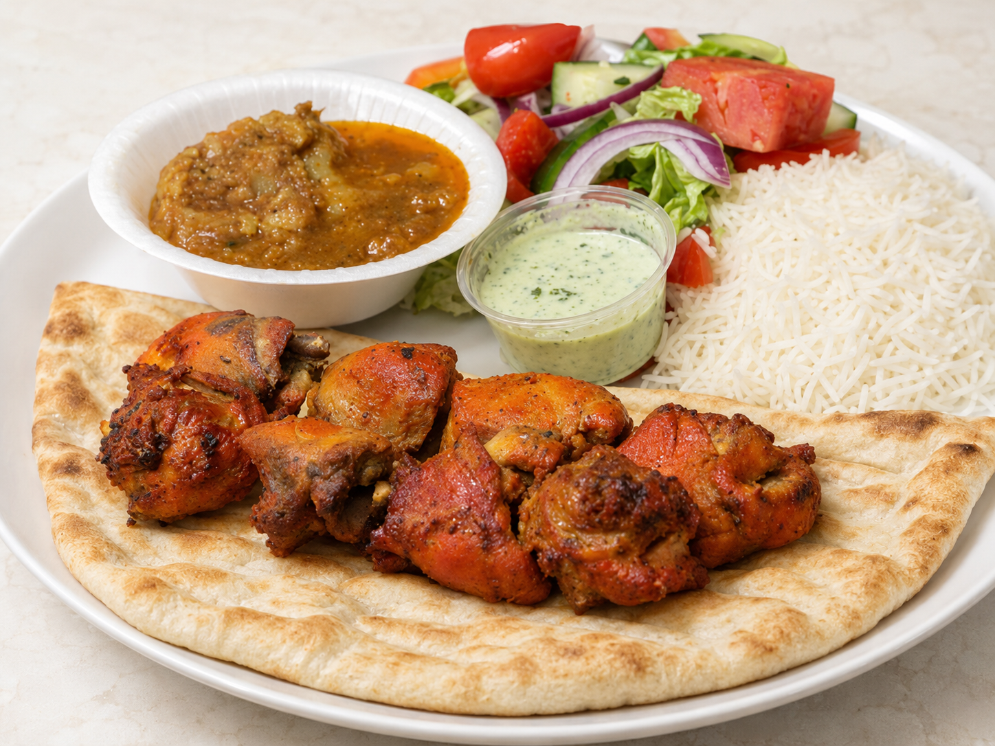 Chicken tikka with naan, rice, curry, chutney, and salad on a white plate