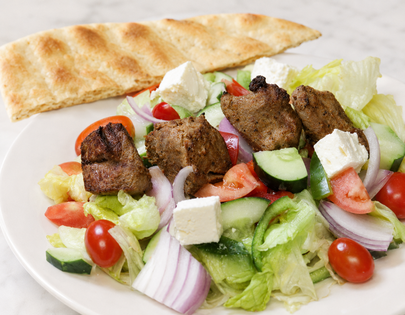 Grilled meat salad with cucumbers, tomatoes, onions, feta, and pita bread on a plate