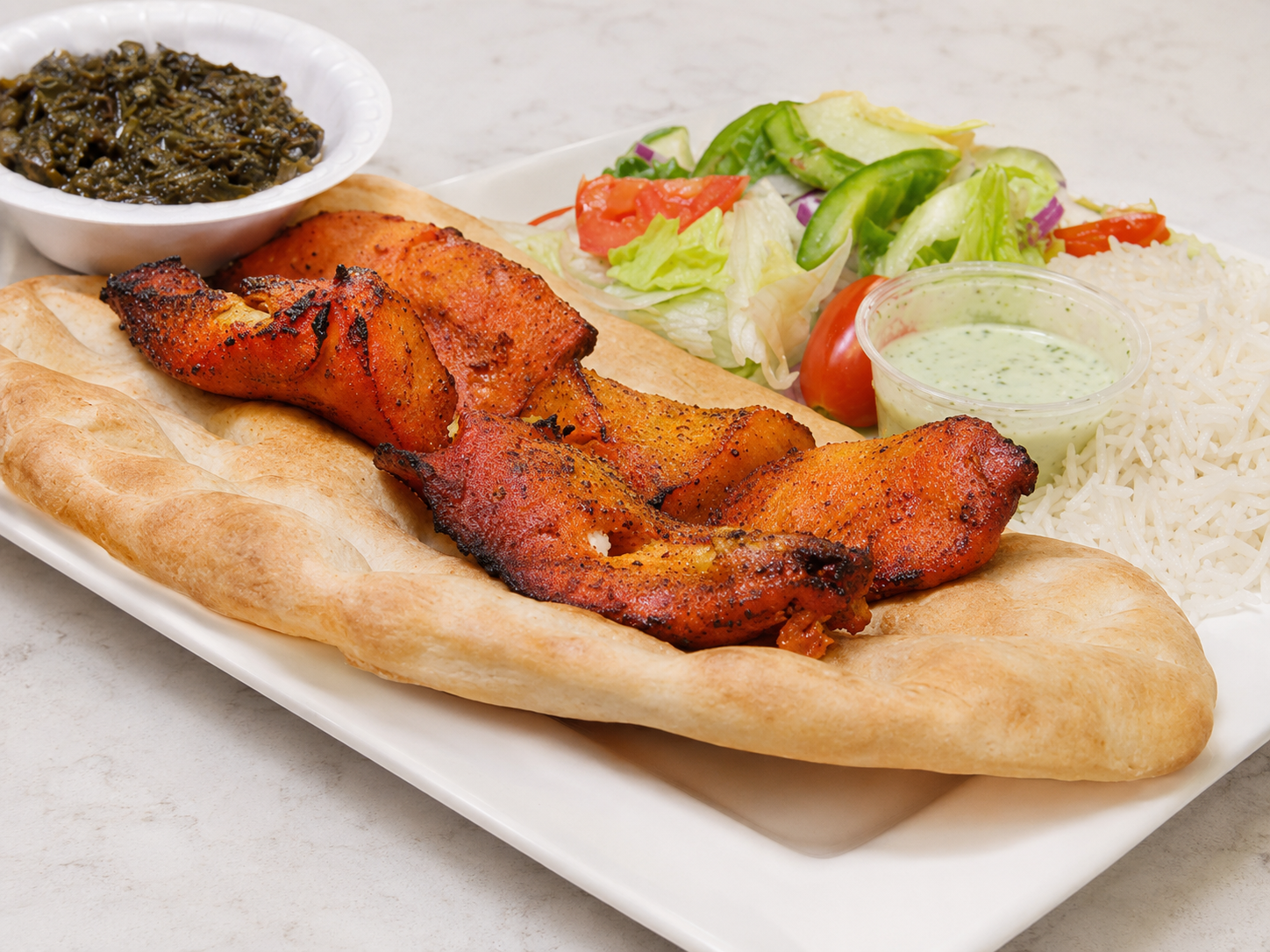 Grilled chicken on flatbread with salad and chutney on a white plate