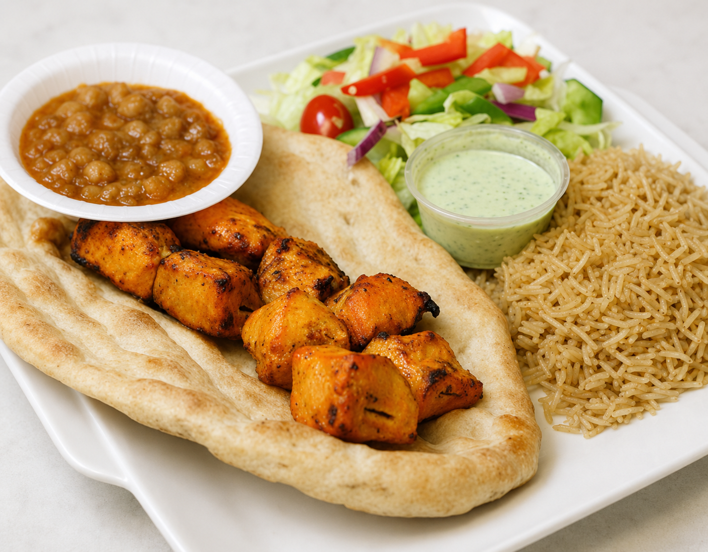 Grilled chicken pita with hummus, salad, lentils, and rice on a white plate