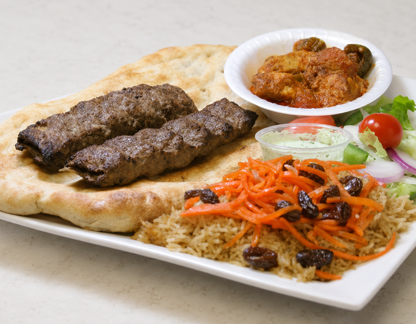 Grilled kebabs with flatbread, rice, salad, and a bowl of stew on a white plate