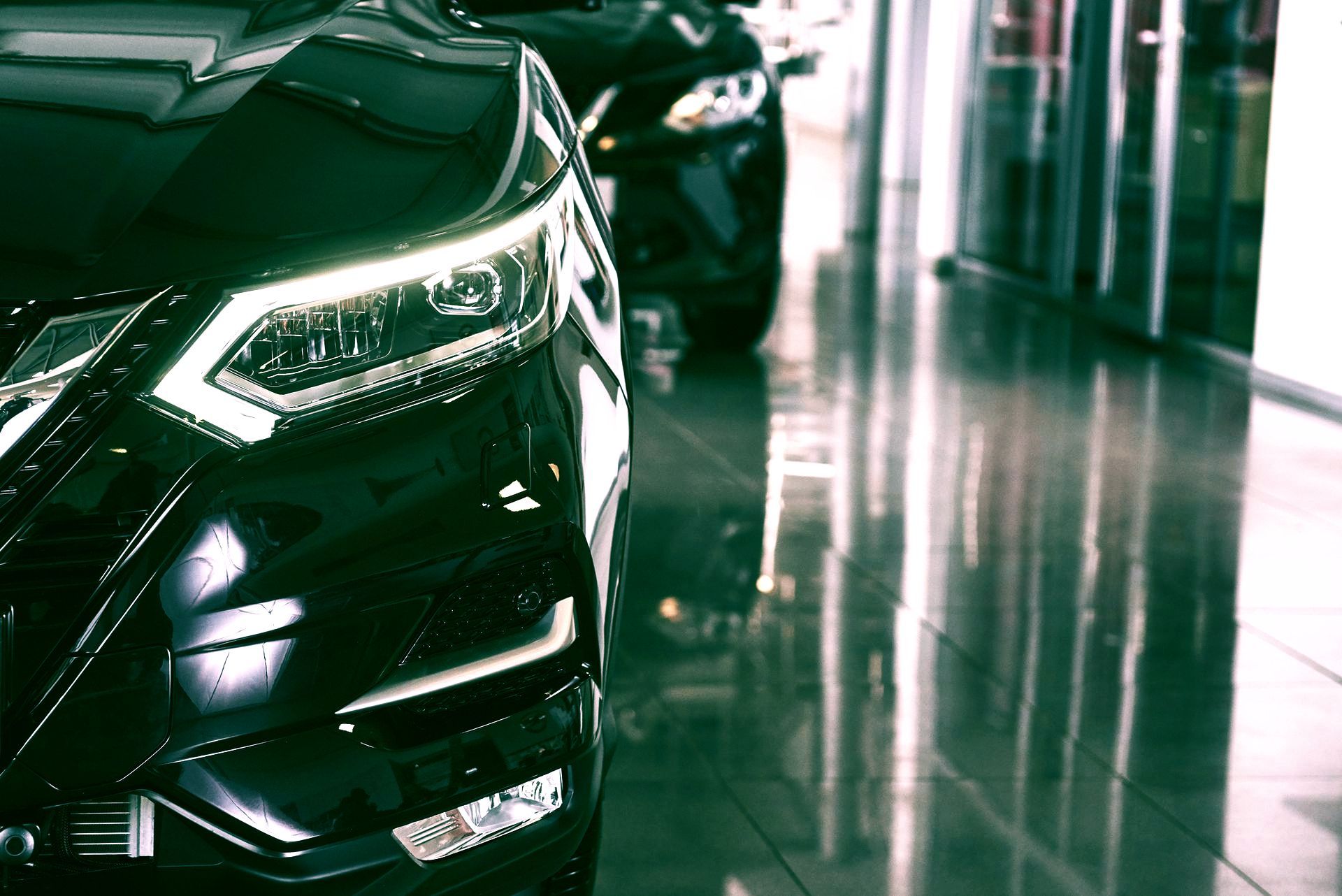 Close-up of a glossy black car in a polished showroom, with bright reflections on the floor and windows.