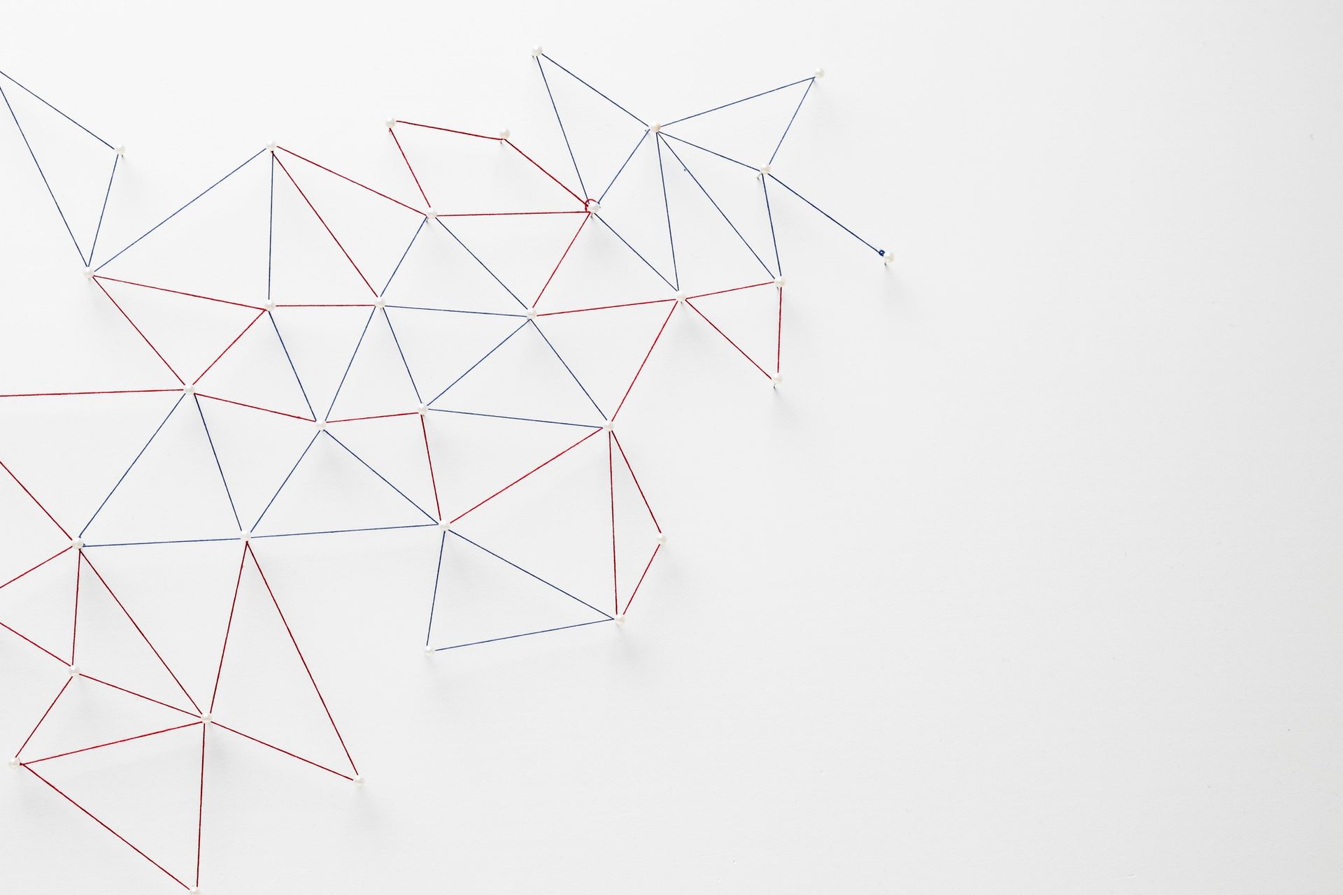 Geometric design on a white background with red and blue thread creating triangular shapes.