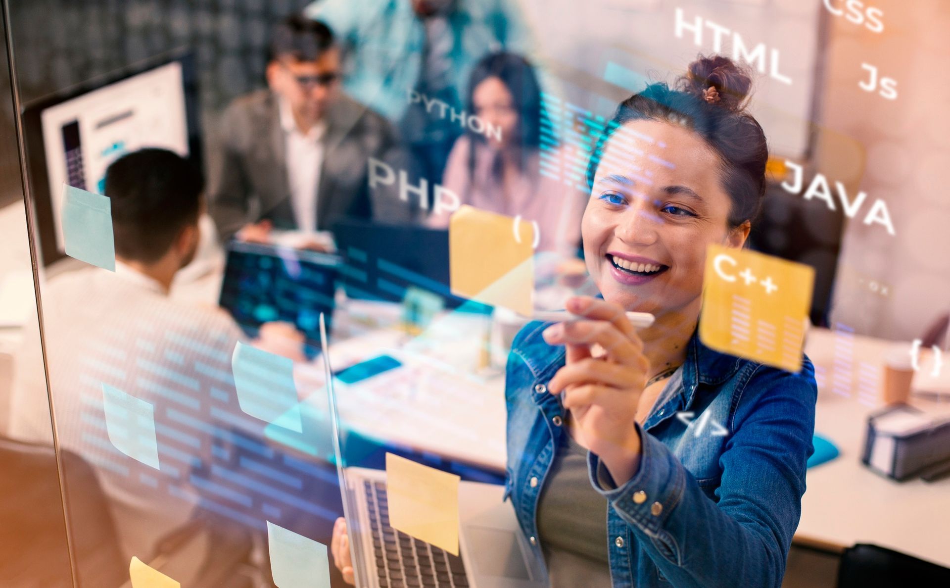 Smiling woman writing on a glass board with programming terms and sticky notes in an office workshop
