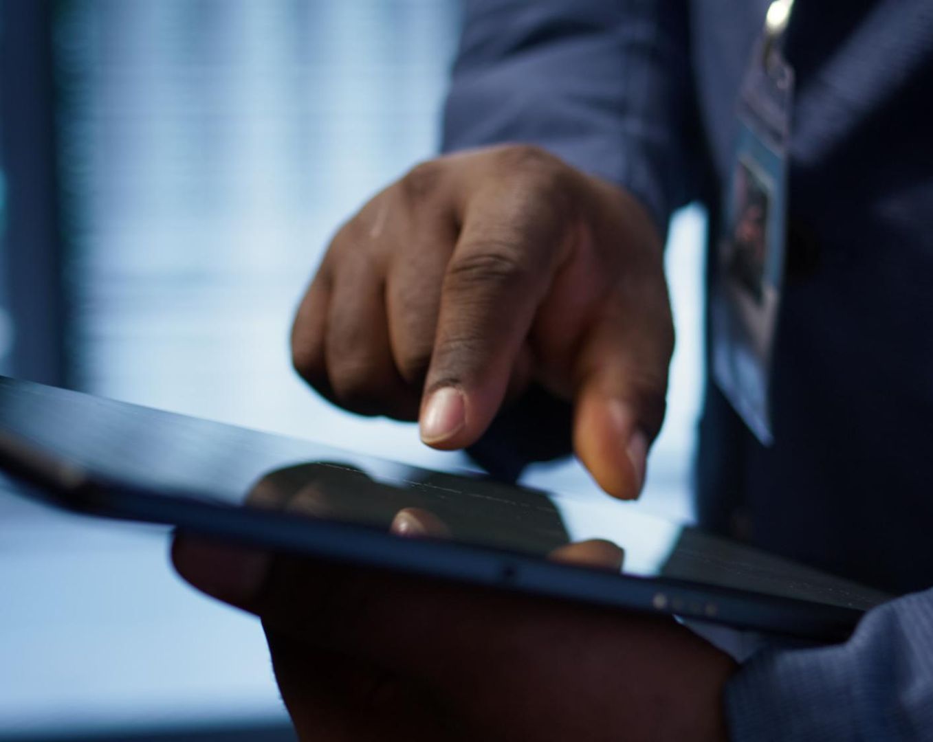 Hand in blue suit tapping a tablet screen with a stylus in a close-up office setting