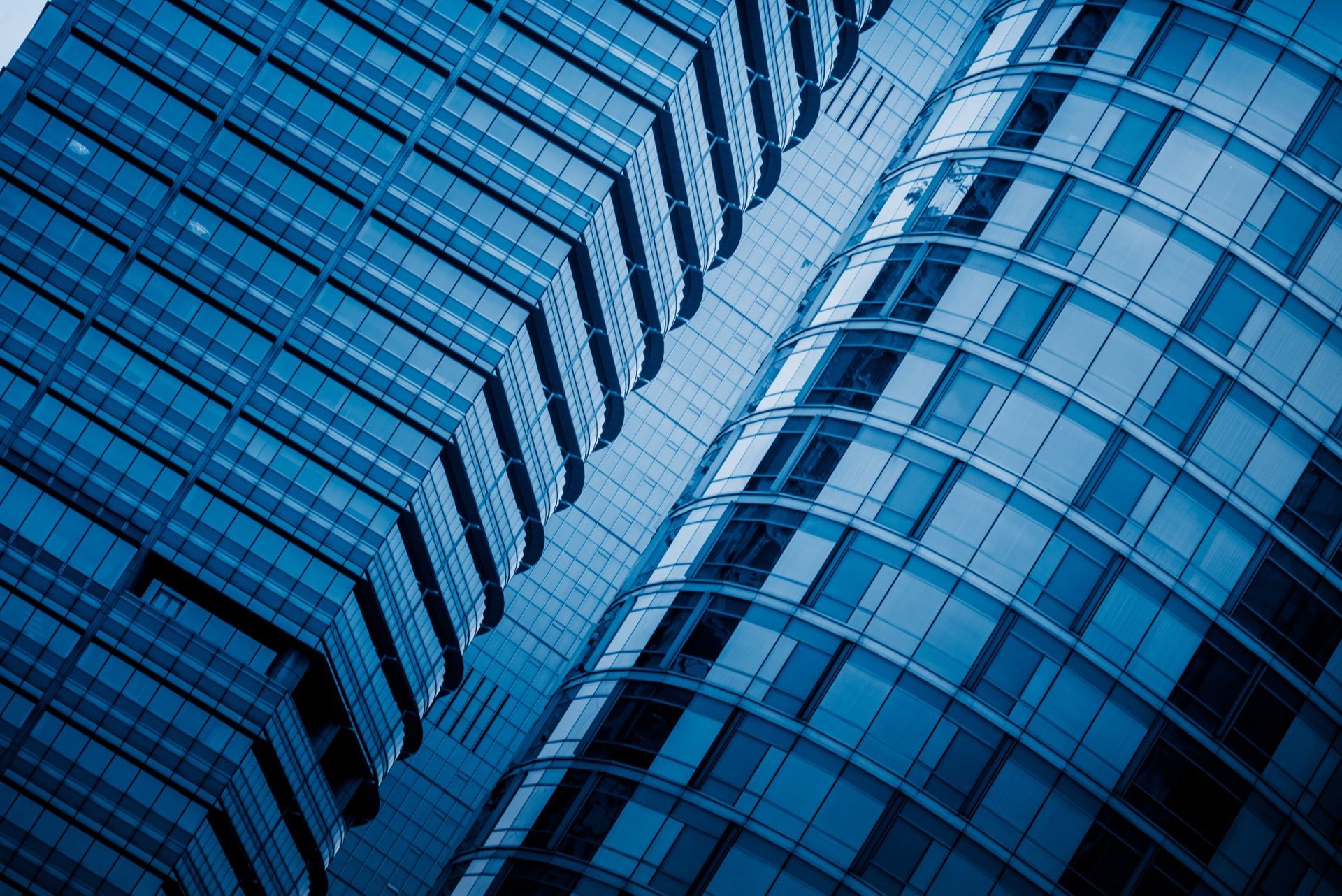 Blue-toned angled view of a skyscraper with a geometric facade and a curved, glass-walled section.