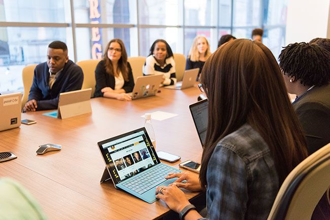 People seated around a conference table in a meeting room, one using a laptop with a presentation on screen