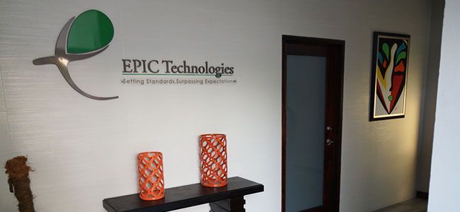 Office lobby with EPIC Technology sign, wall art, and a dark door beside a small table with two orange lamps.