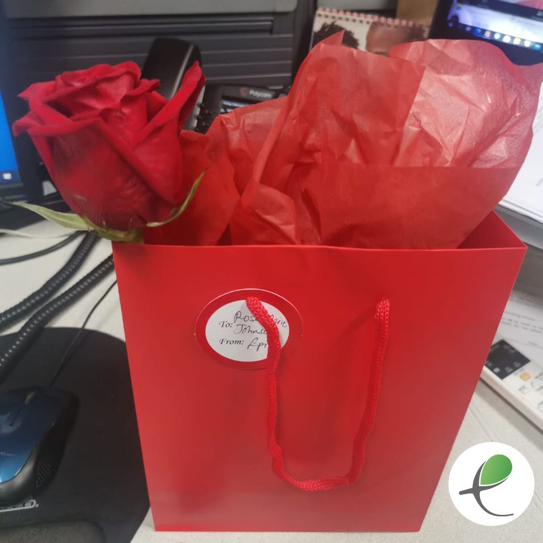 Red gift bag with a rose sticking out, sitting on a desk.