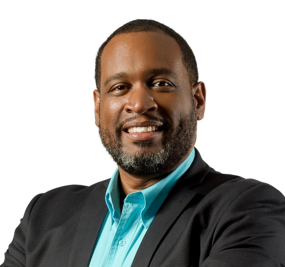 Smiling man in a black blazer and teal shirt against a white background
