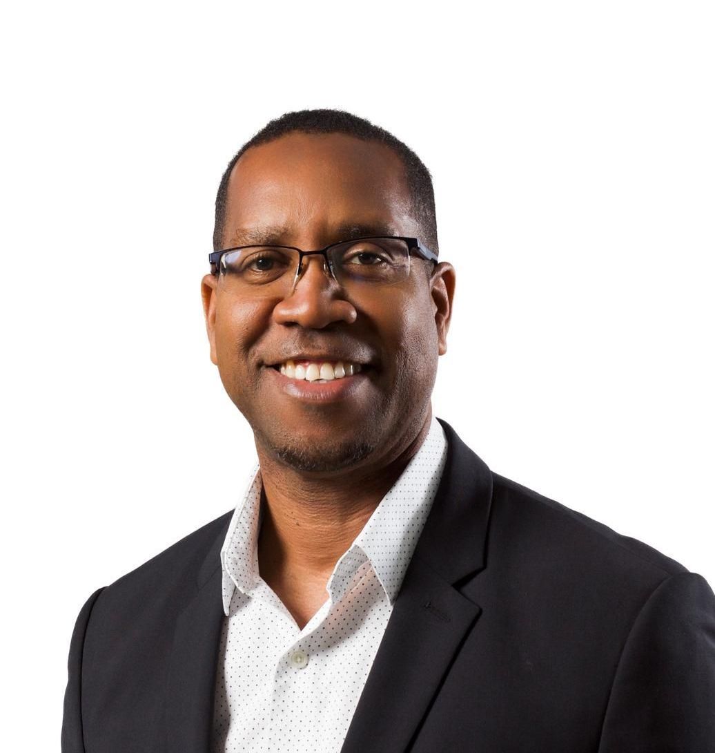 Smiling man in glasses wearing a dark blazer and white shirt against a white background