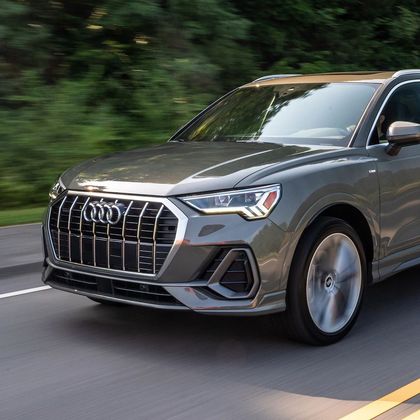 Gray Audi SUV driving on a road, with blurred green trees in the background.
