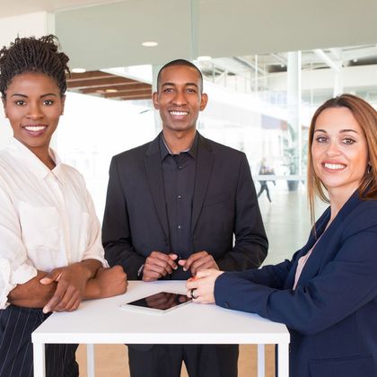 Three professionals standing together in a bright office, smiling around a white table.