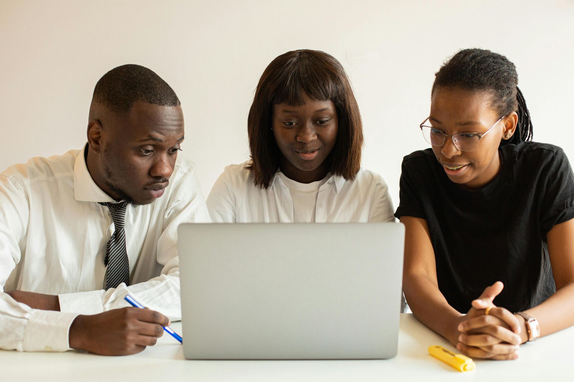 Three coworkers leaning over a laptop in a meeting, discussing notes at a white table