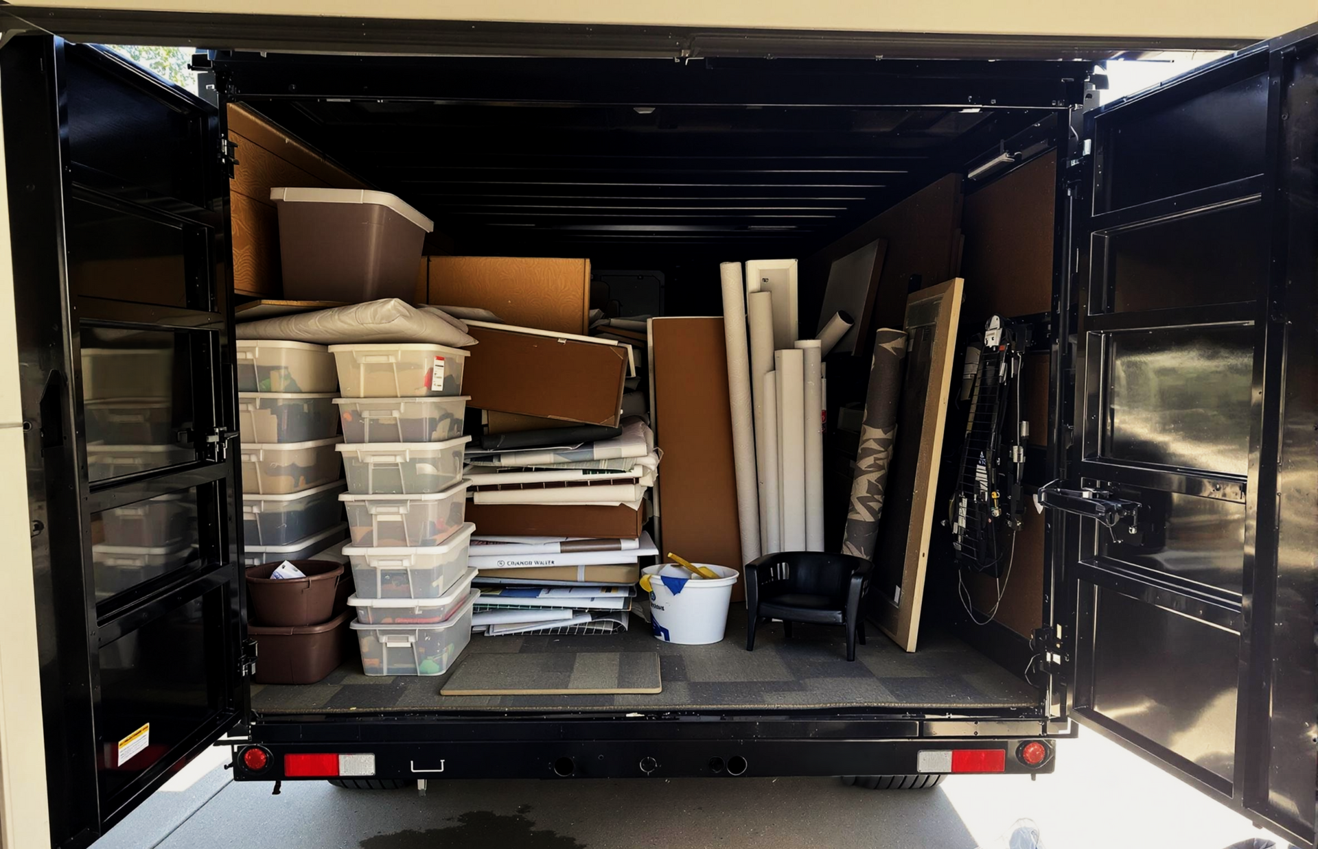 A truck's cargo bay loaded with boxes, boards, and various items, doors open.