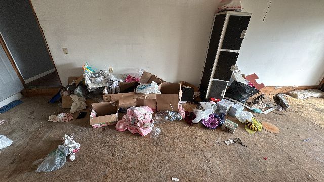 Cluttered room with trash, boxes, and a cabinet. Dirty floor and walls.