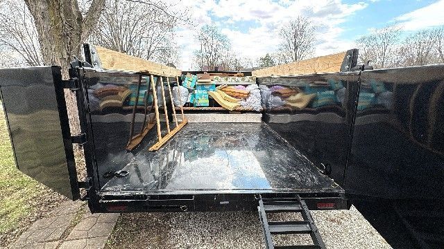 Open black trailer loaded with various household items; ramp extended.