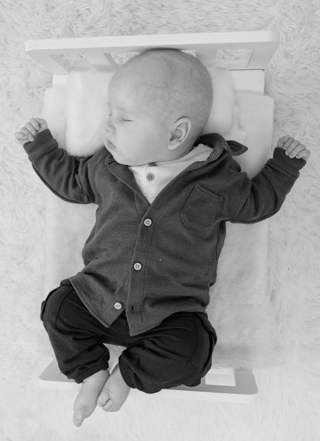A black and white photo of a baby laying on a bed.