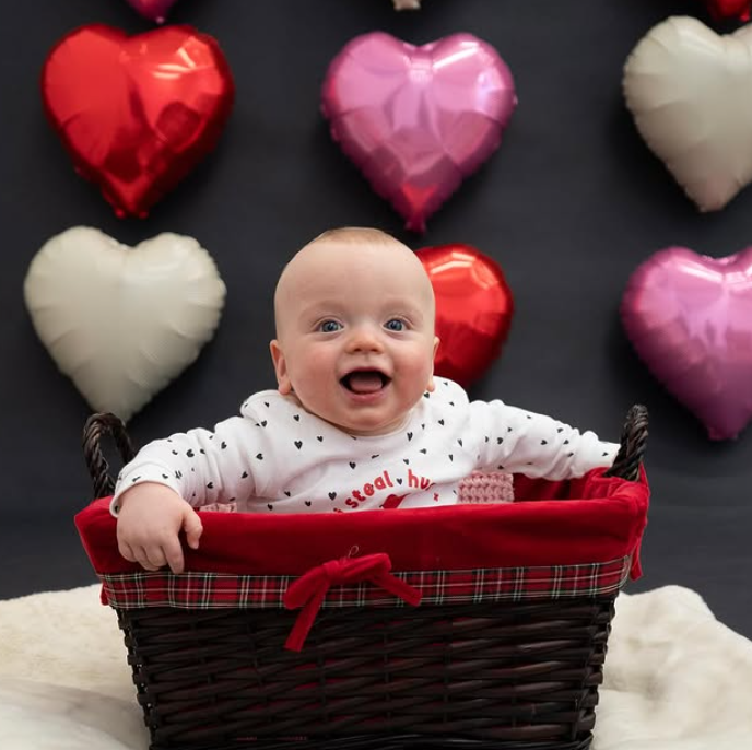 A baby is sitting in a basket with hearts in the background