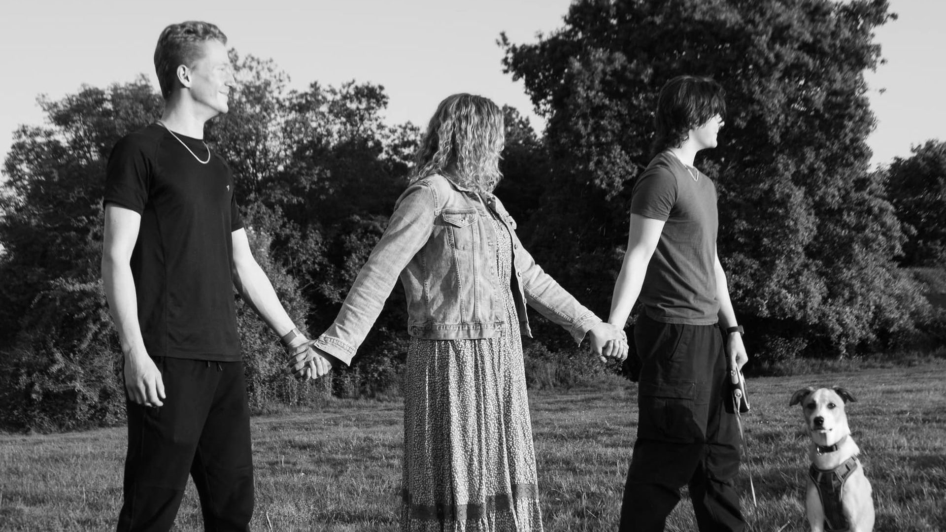 A group of people holding hands in a field with a dog.