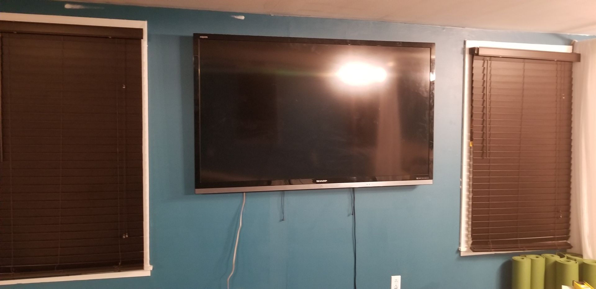 A large flat screen tv is hanging on a wall next to two windows.