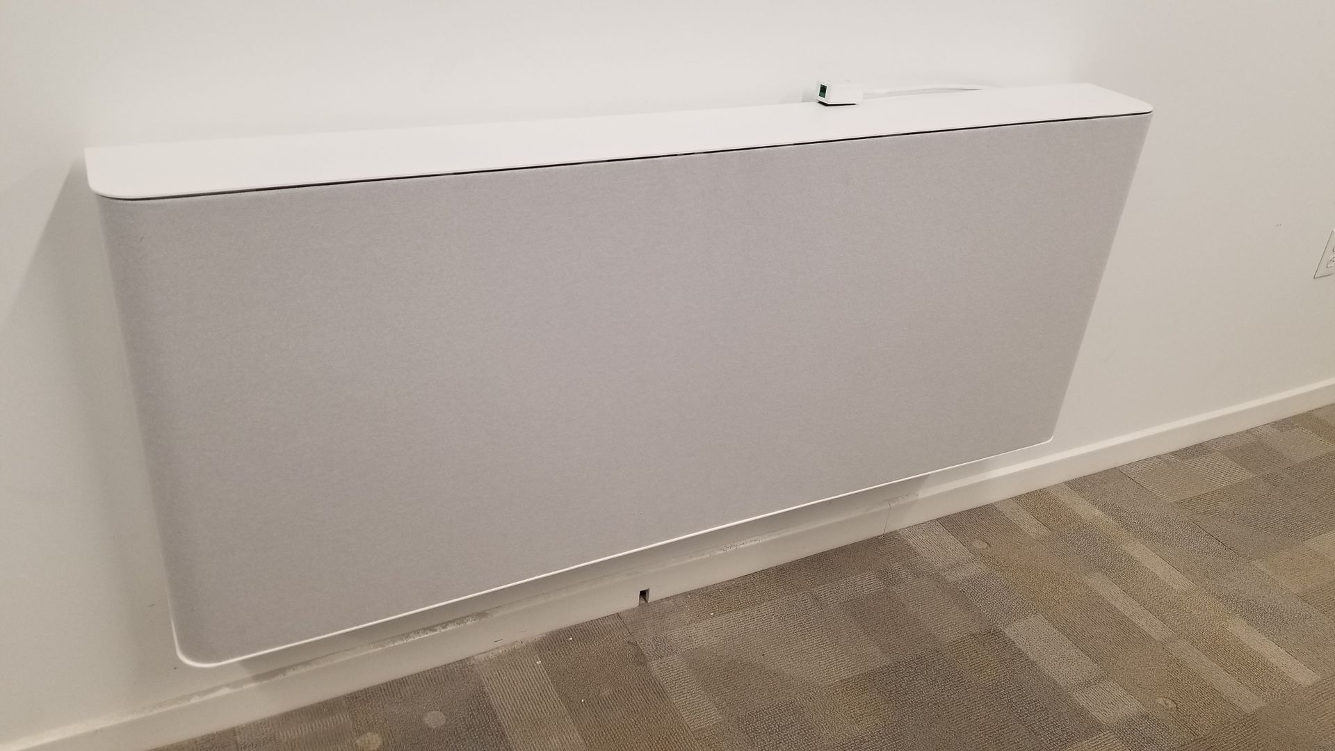 A white box is hanging on a wall next to a carpeted floor.