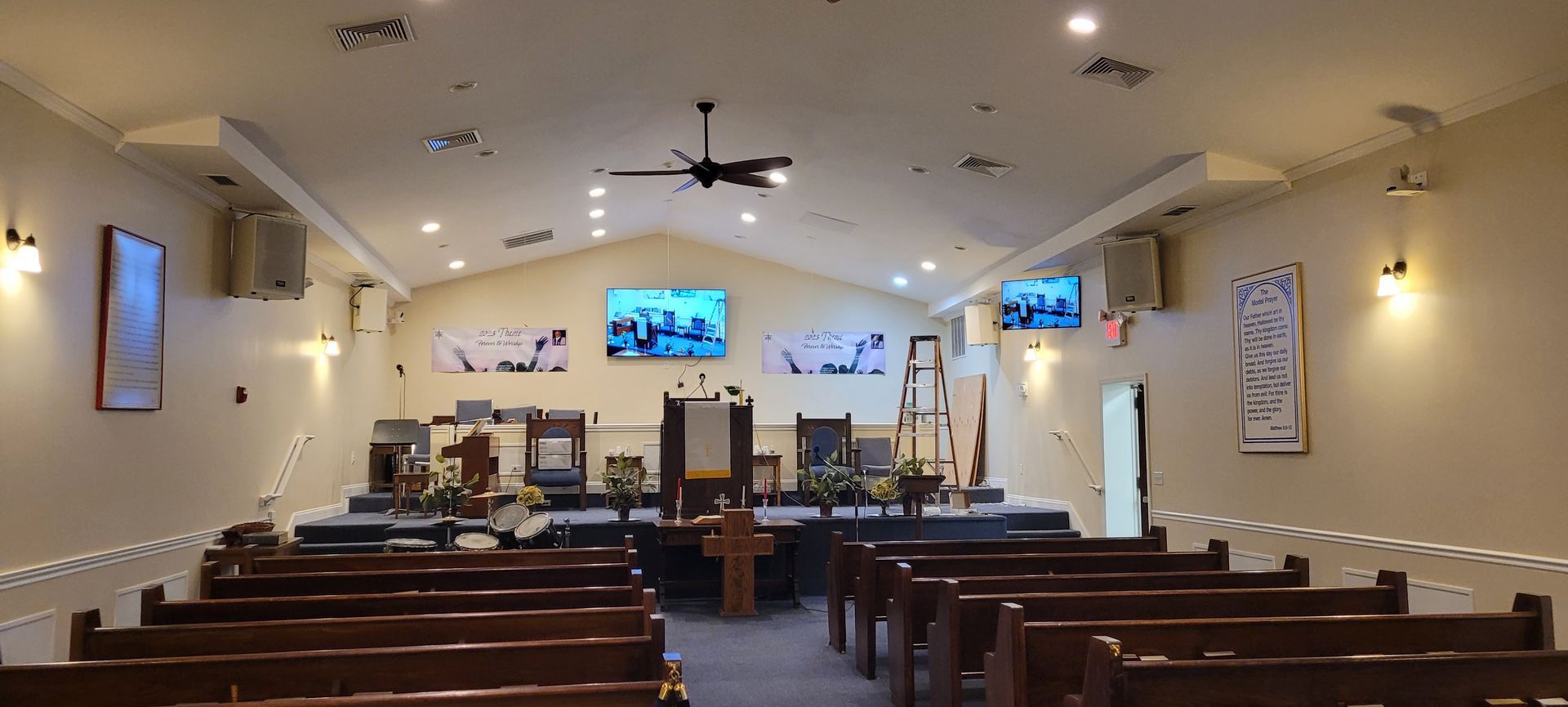 A church with rows of wooden benches and a ceiling fan.