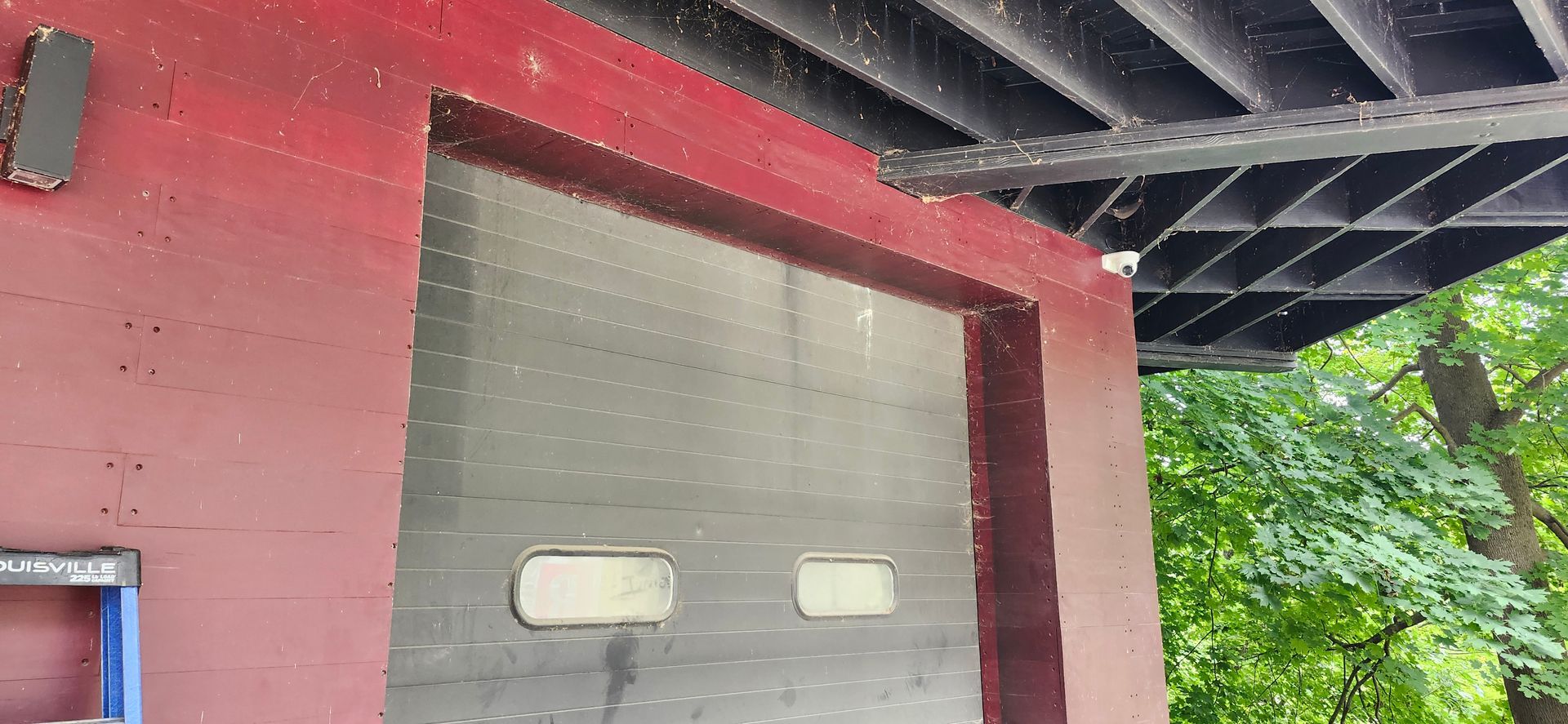 A red building with a garage door under a bridge.
