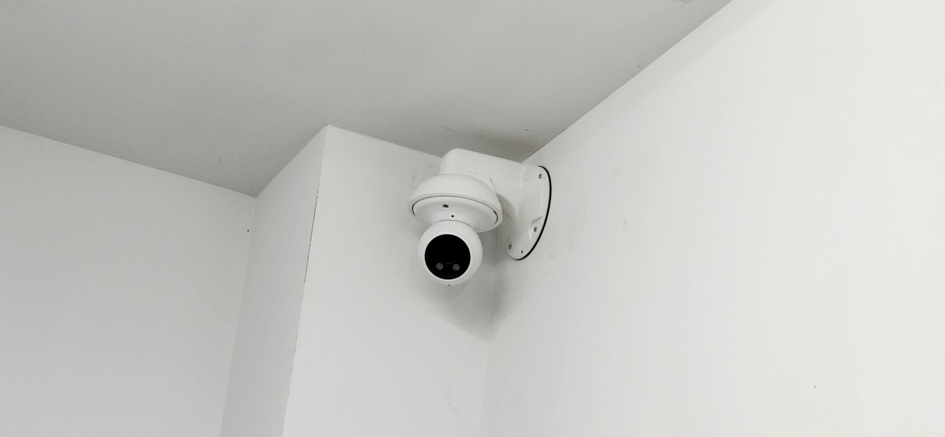 A security camera is mounted on the corner of a white wall.