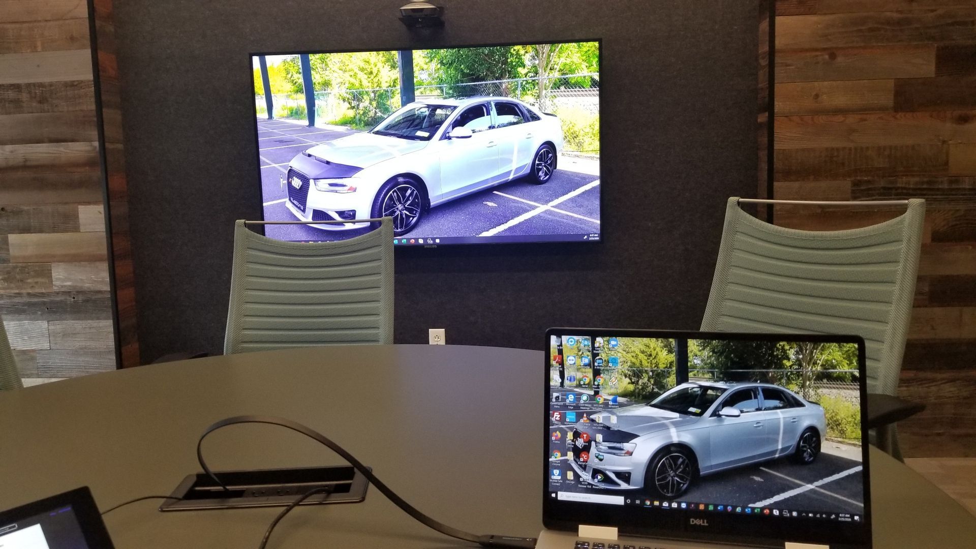 A white car is displayed on a flat screen tv in a conference room.
