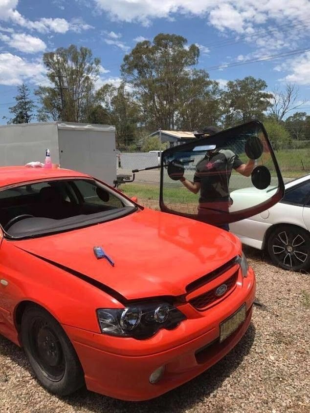 A Person Replacing the Windshield on a Bright Orange Car Outdoors — Road Runner Windscreens in South Grafton, NSW