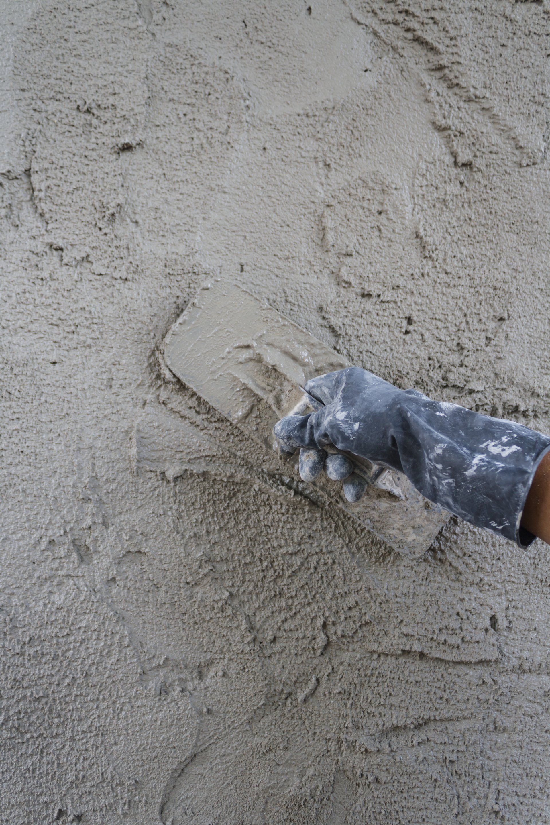 A gloved hand smooths wet gray cement with a trowel on a construction surface.