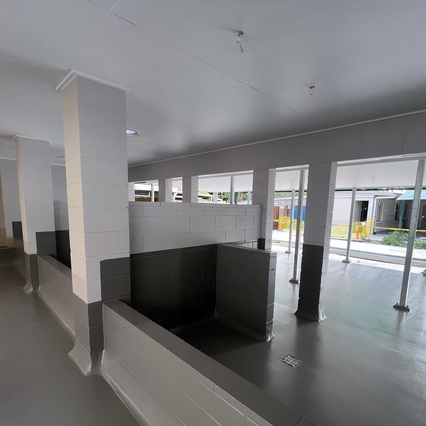 Empty modern interior with white columns, gray floor, and black partition walls, lit by large windows
