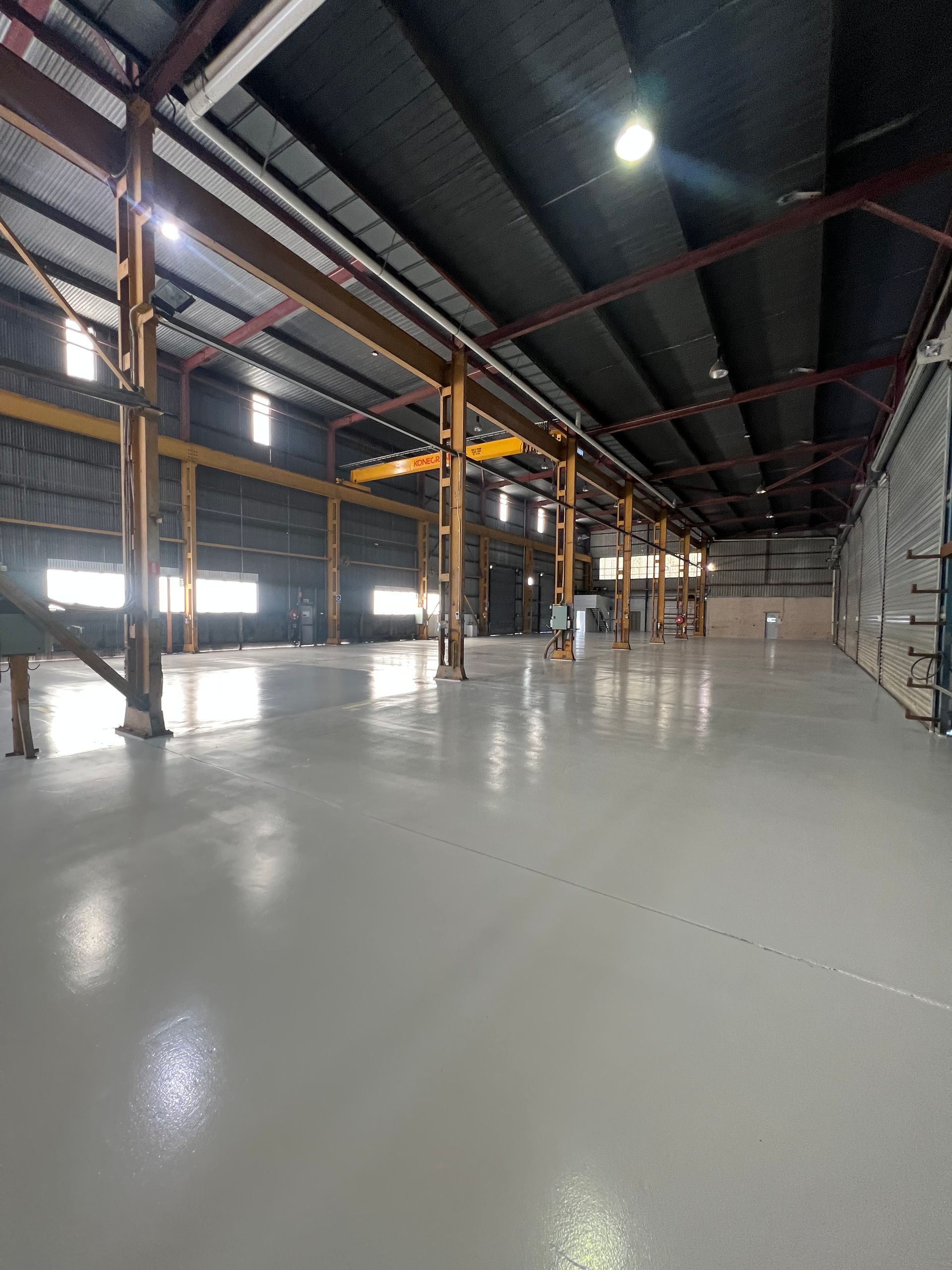 Empty industrial warehouse with polished concrete floor, steel beams, and skylights overhead.