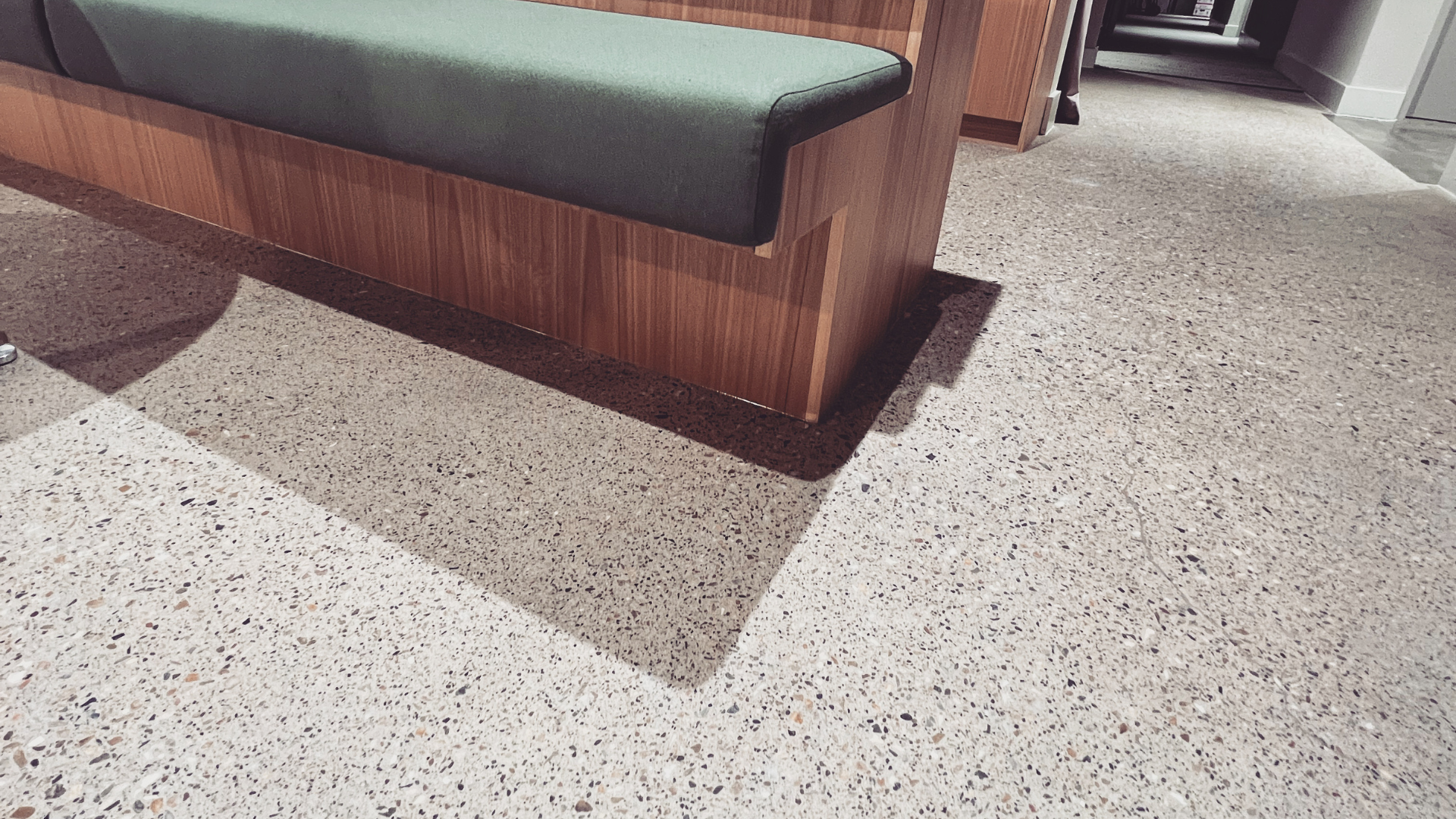 Wooden bench with a green cushion on a speckled concrete floor in a bright indoor lobby Wooden bench with a green cushion on a speckled concrete floor in a bright indoor lobby