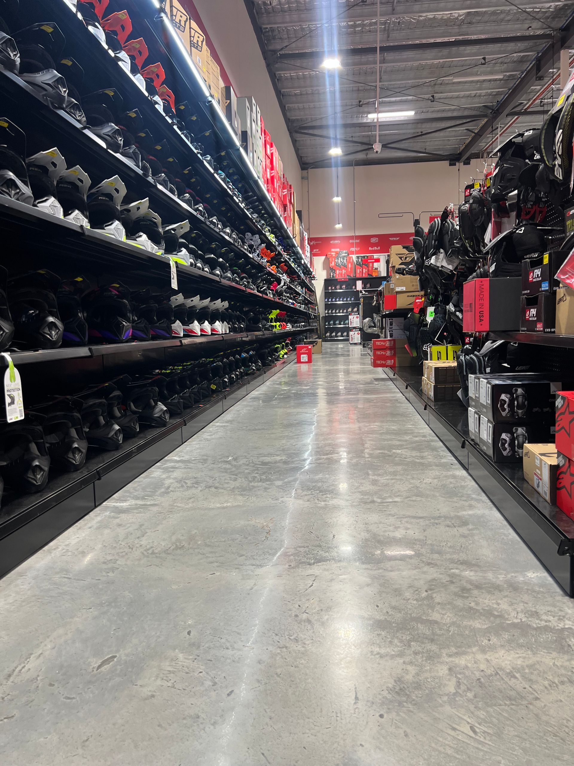 A retail store aisle lined with shoes on tall shelves under bright overhead lights.